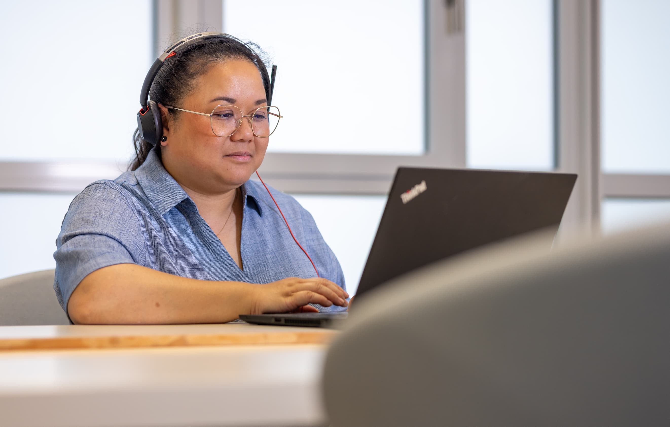 Eine Kollegin sitzt im M-net-Büro vor dem Laptop, sie hat ein Headset auf dem Kopf