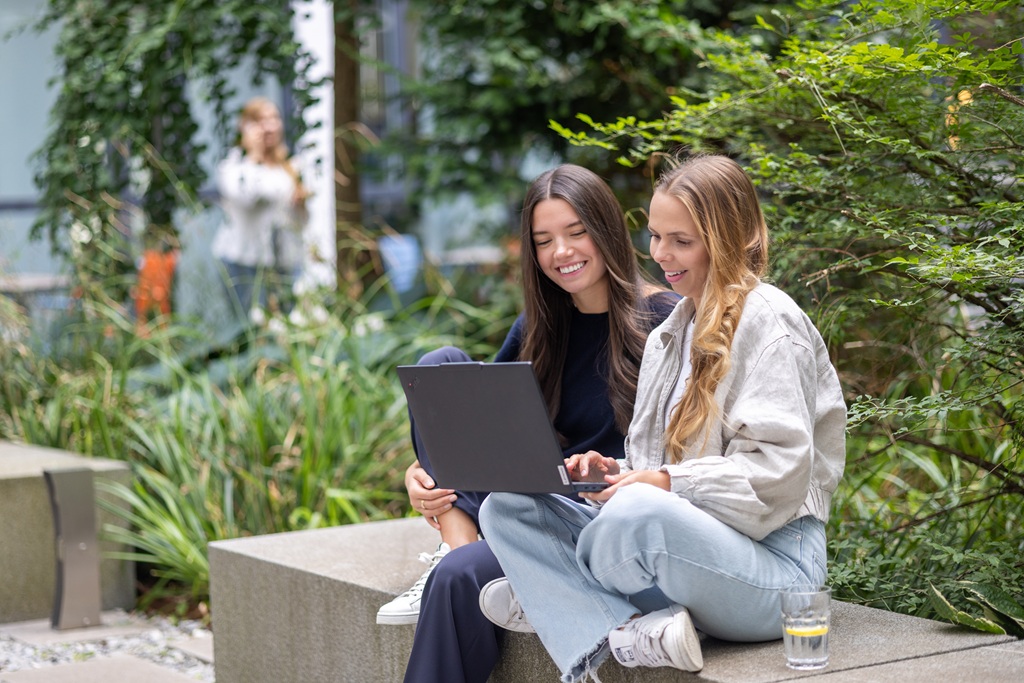 Zwei Mitarbeiterinnen von M-net sitzen im Freien gemeinsam vor einem Laptop