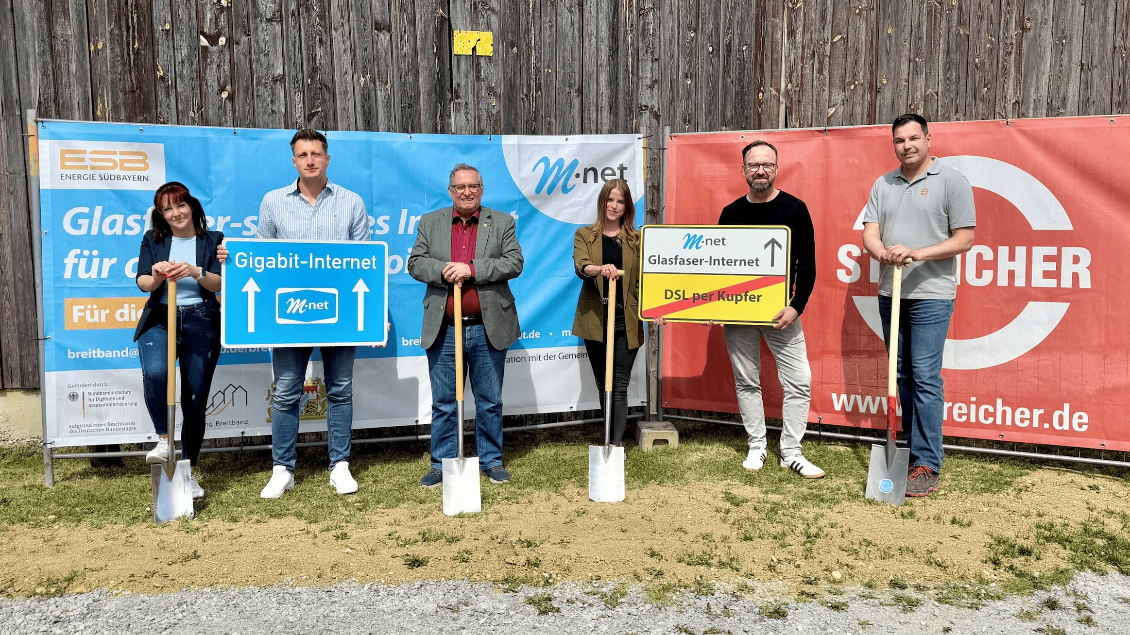 Vertreter von M-net, ESB und der Gemeinde Loiching vor Plakaten und mit Schildern in der Hand.