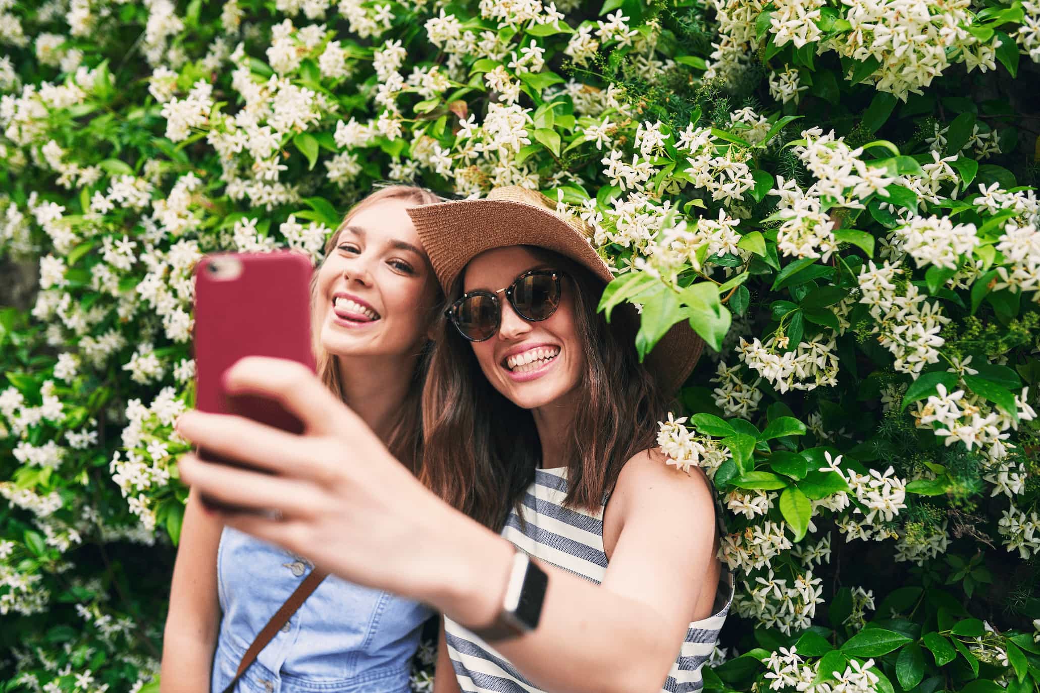 Zwei Frauen vor einer Hecke machen ein Selfie voneinander