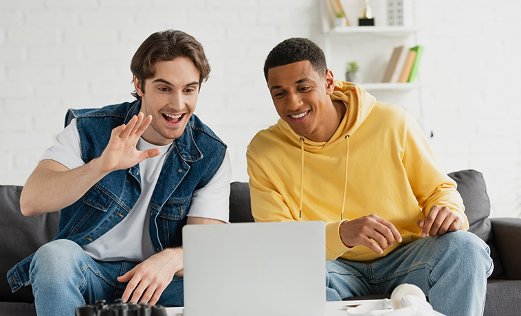 Zwei Männer auf einem Sofa vor einem Laptop scheinbar bei einem Videocall