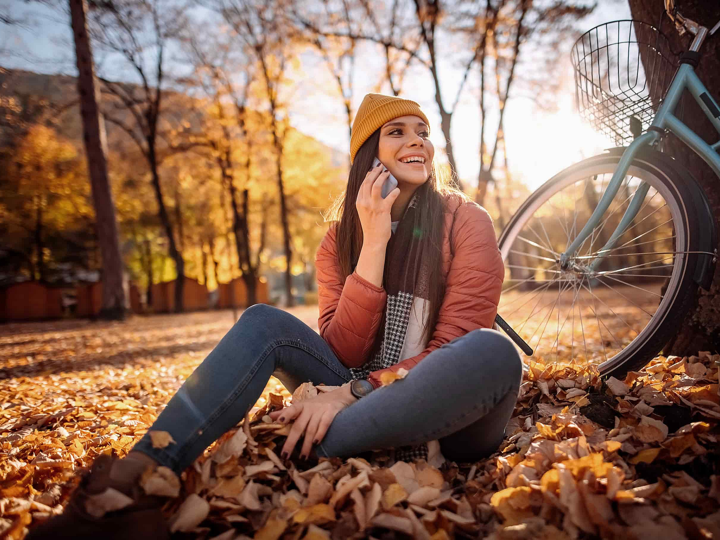 Eine Frau sitzt auf dem Waldboden und telefoniert mit dem Handy