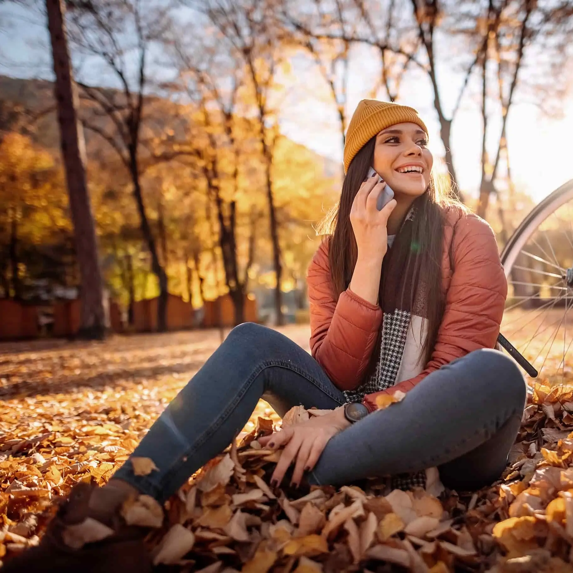 Eine Frau sitzt auf dem Waldboden und telefoniert mit dem Handy