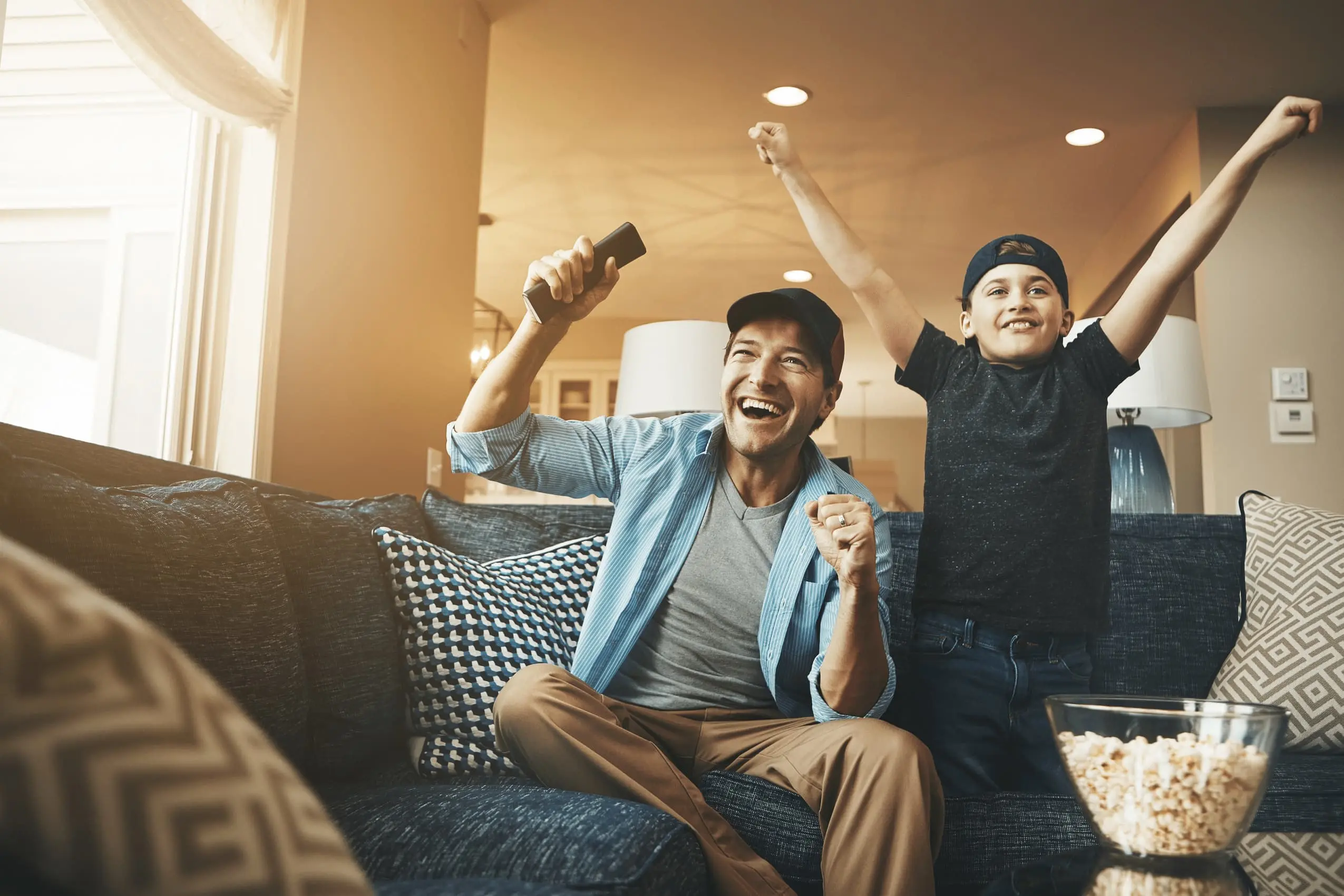 Vater und Sohn sitzen jubelnd auf der Couch vor dem Fernseher.