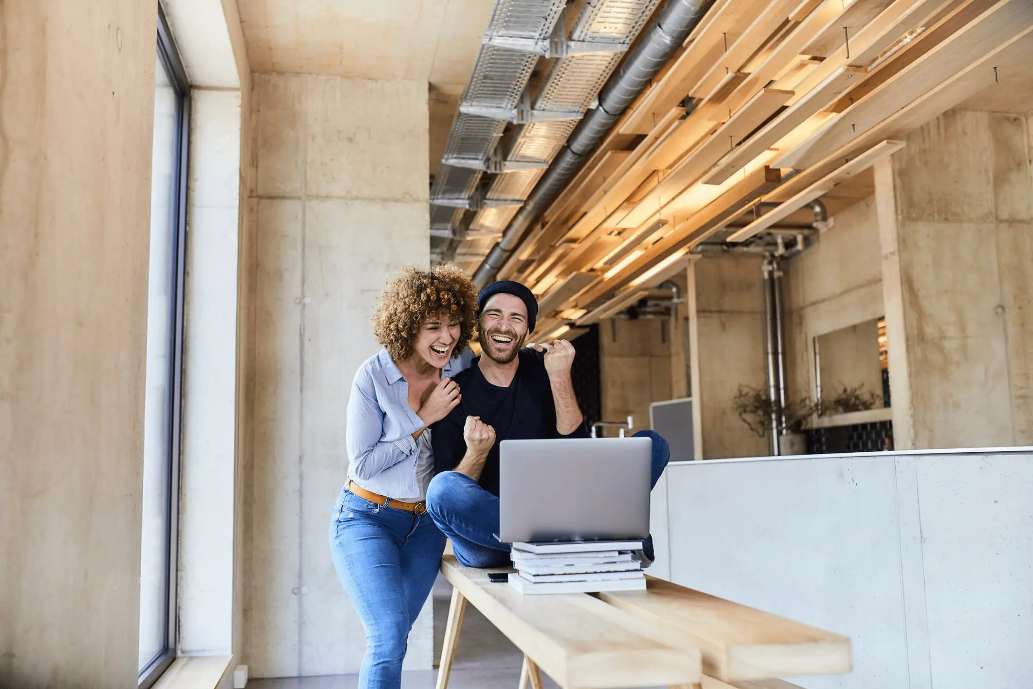 Eine Frau und ein Mann stehen in einem loft-artigen Wohnzimmer vor dem Laptop.
