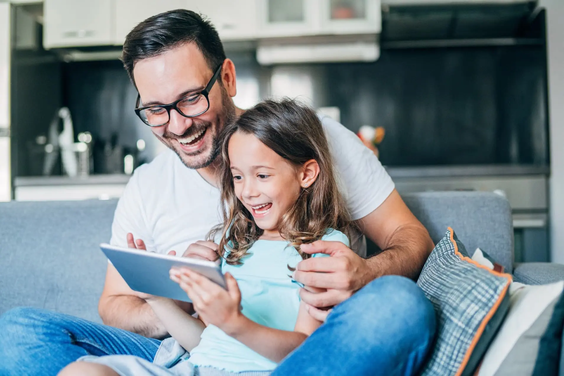 Ein Vater sitzt gemeinsam mit seiner kleinen Tochter vor einem Tablet