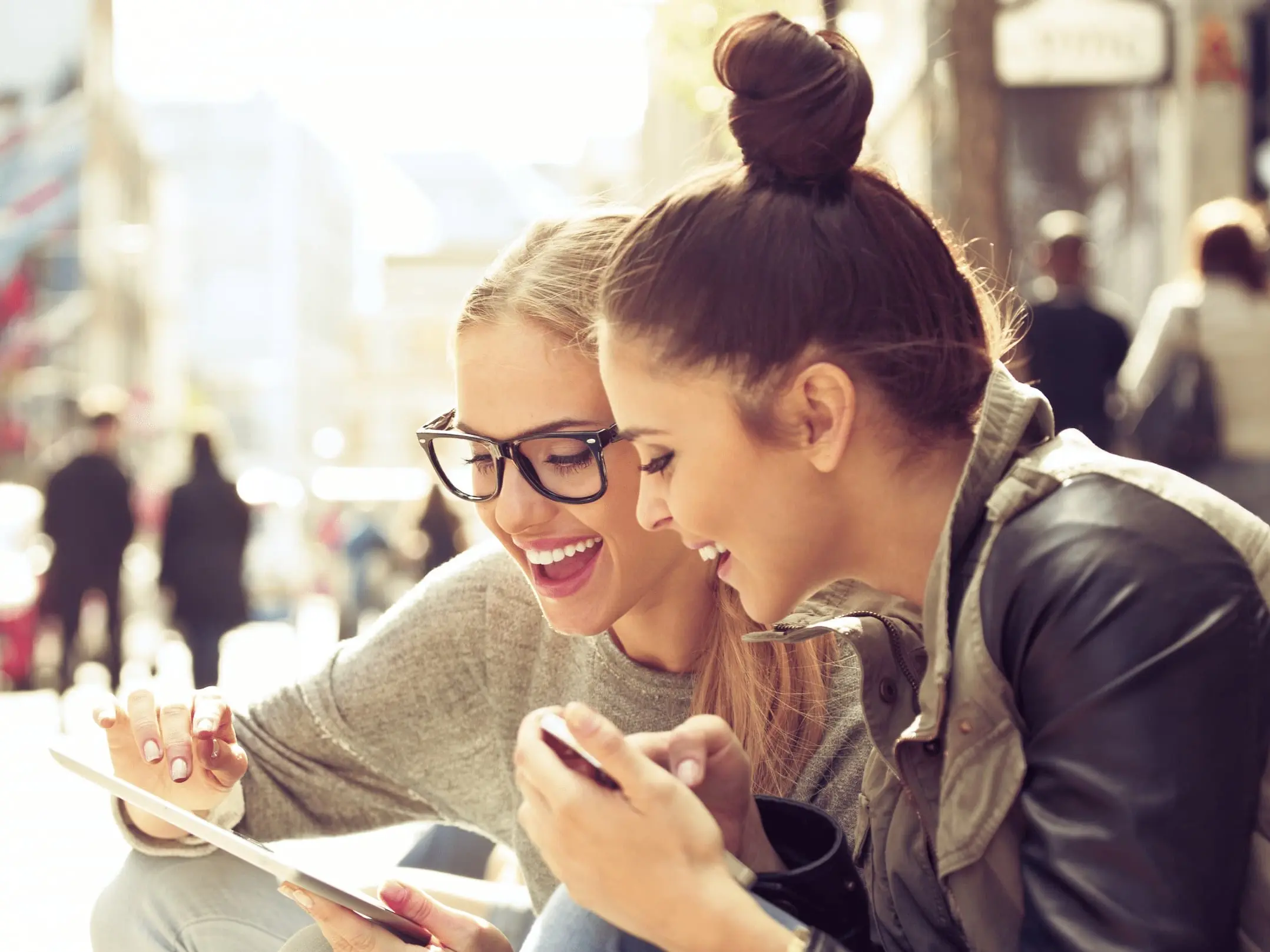 Zwei Frauen sitzen drau&szlig;en und schauen gemeinsam in ein Tablet