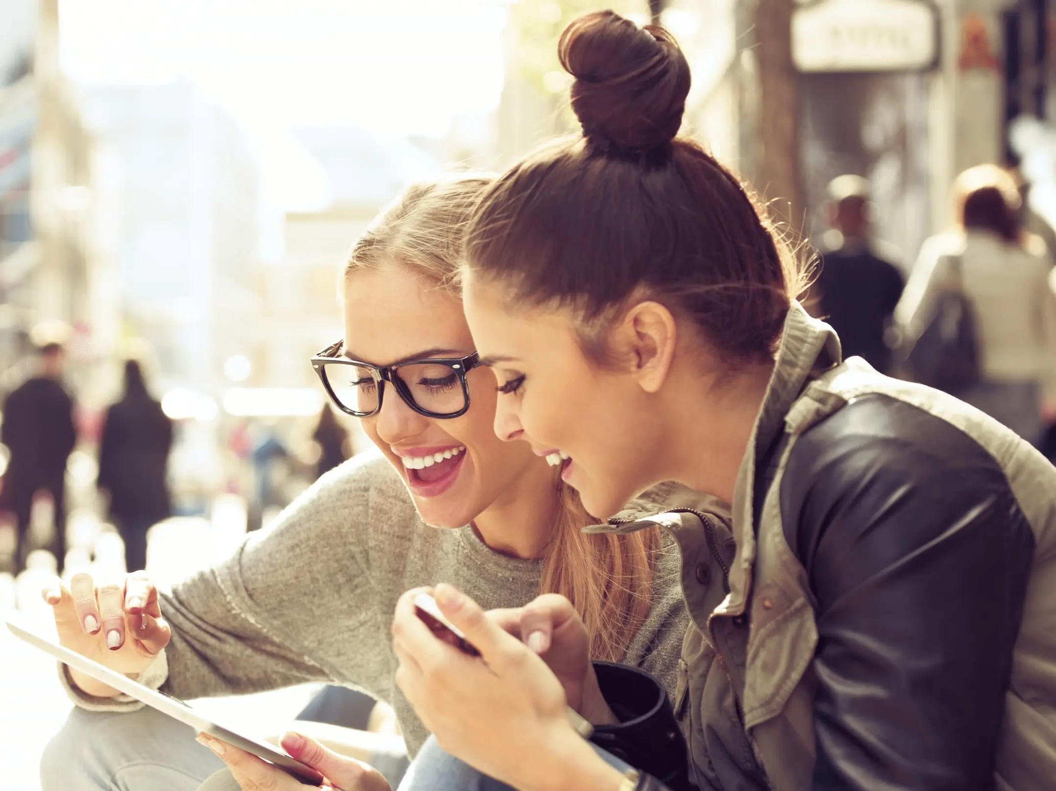 Zwei Frauen sitzen drau&szlig;en und schauen gemeinsam auf ein Tablet