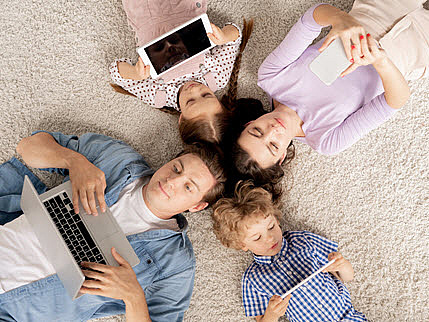 Eine Familie auf dem Boden liegend, jeder mit einem Endgerät in der Hand, Vogelperspektive