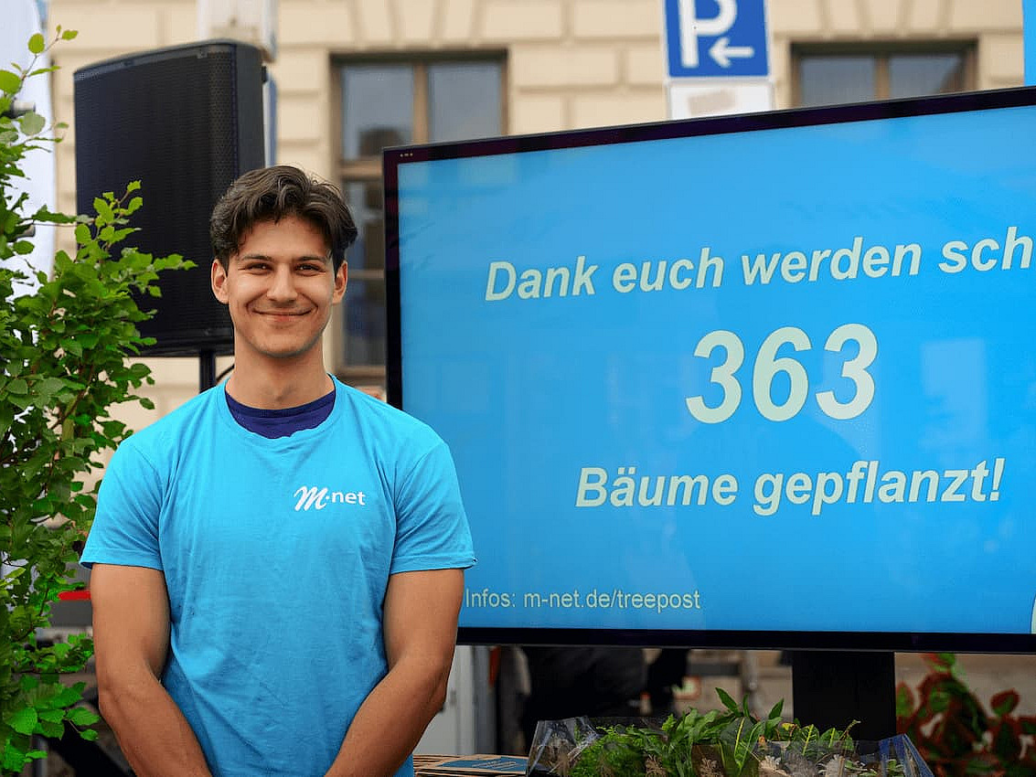 Mitarbeiter vor einem Infoscreen, auf dem die Anzahl der gepflanzten Bäume zu lesen ist