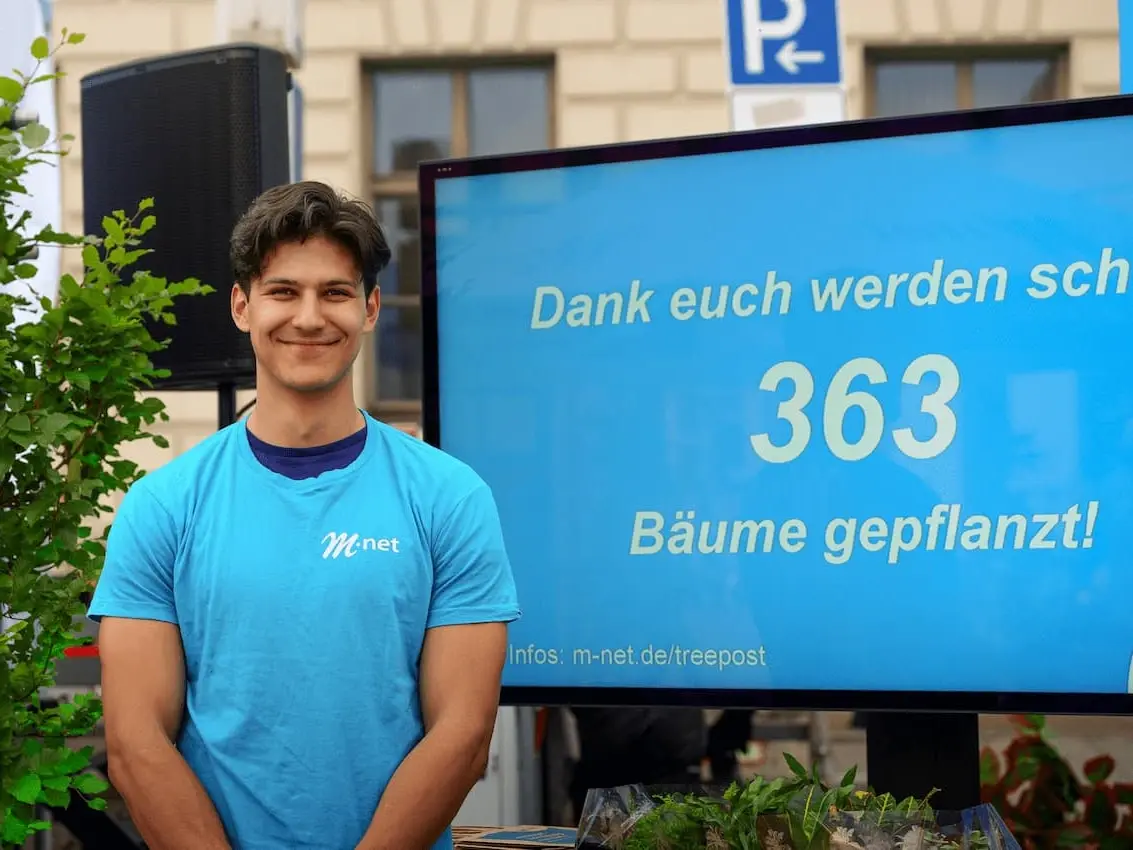 Mitarbeiter vor einem Infoscreen, auf dem die Anzahl der gepflanzten Bäume zu lesen ist