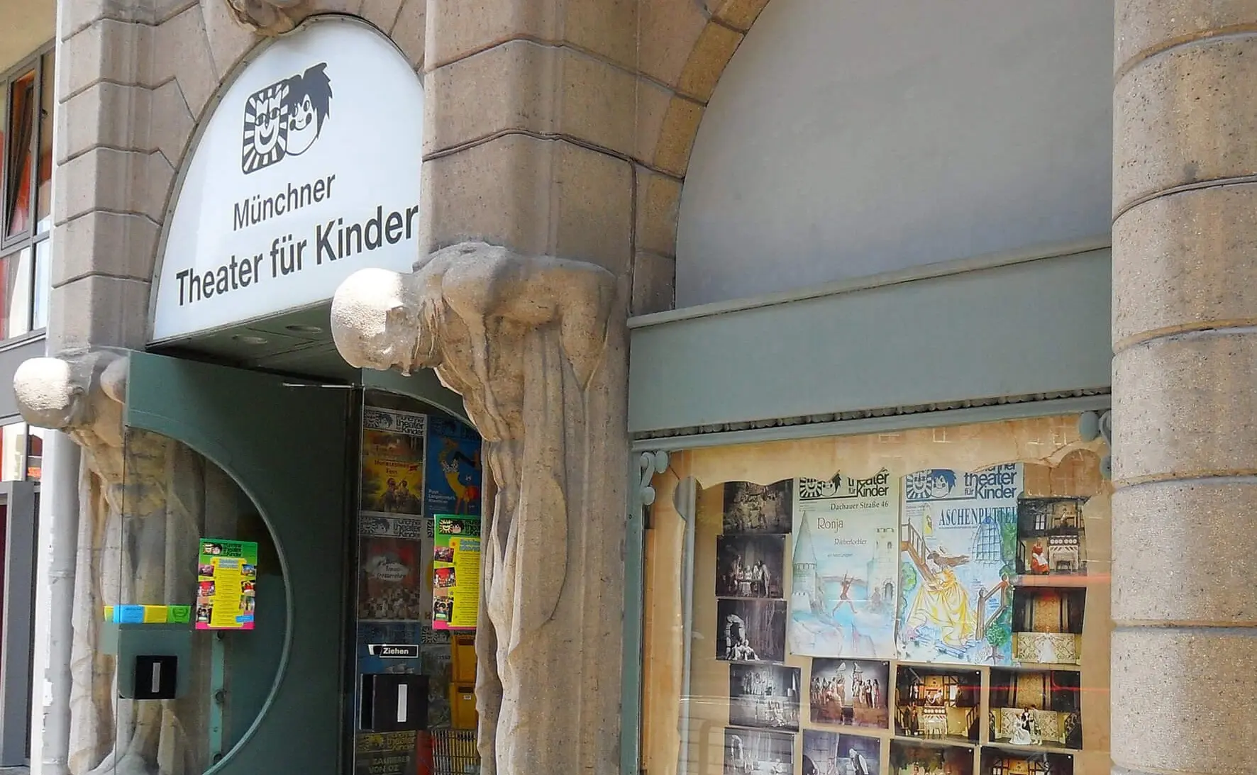 Zu sehen ist das Münchner Traditionstheater für Kinder von Außen. Man kann den Eingang zum Theater sowie das rechte Schaufenster daneben sehen.