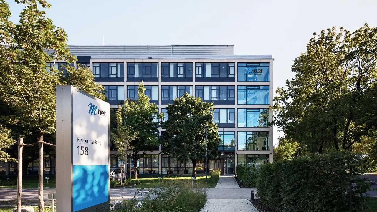 Zu sehen ist das M-net Firmengebäude von außen umgeben von grünen Bäumen
