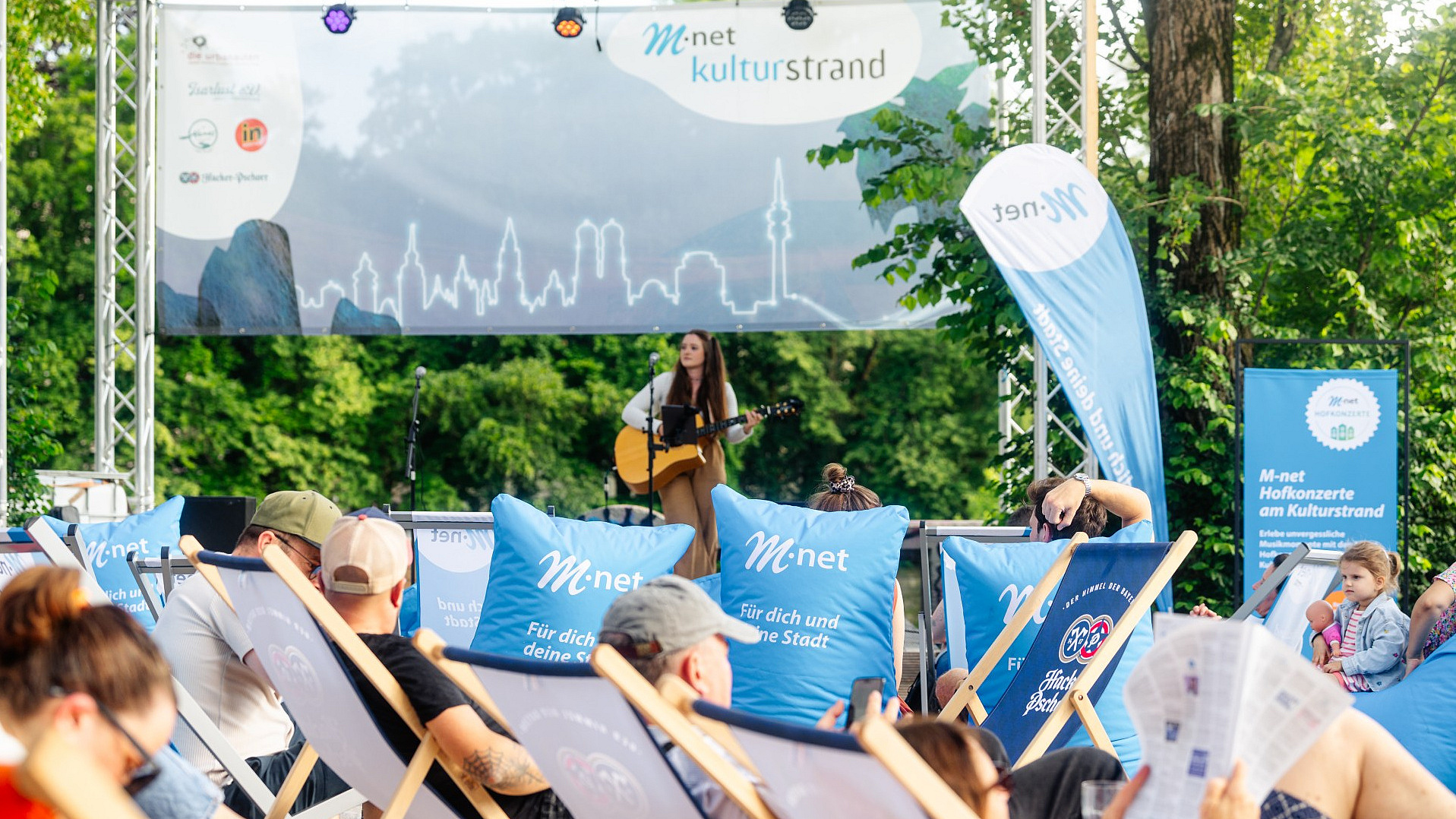 Eine Sängerin die auf dem Hofkonzert Gitarre spielt. Zu sehen ist außerdem die M-net Lounge.