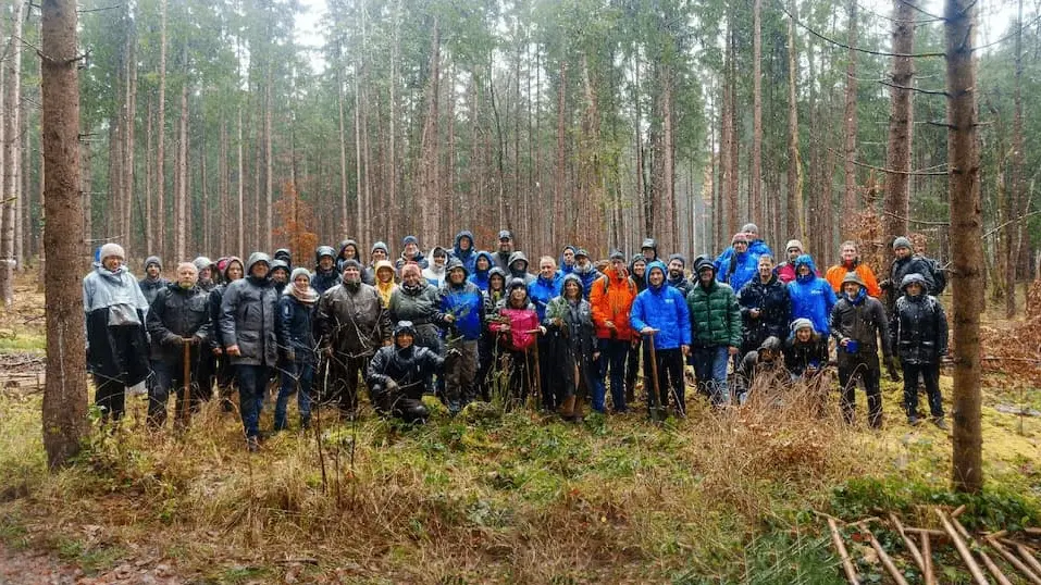 Eine Gruppe an M-net Mitarbeitern steht im Wald bei letzten Baumpflanzaktion.