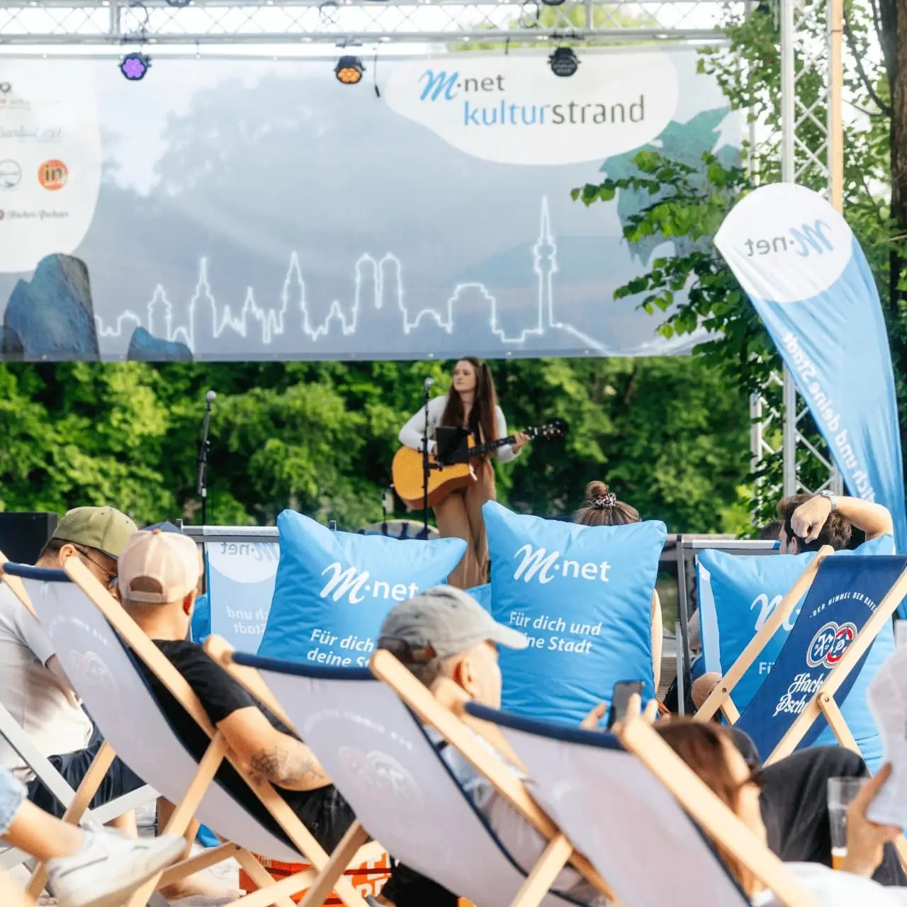 Eine Sängerin die auf dem Hofkonzert Gitarre spielt. Zu sehen ist außerdem die M-net Lounge.