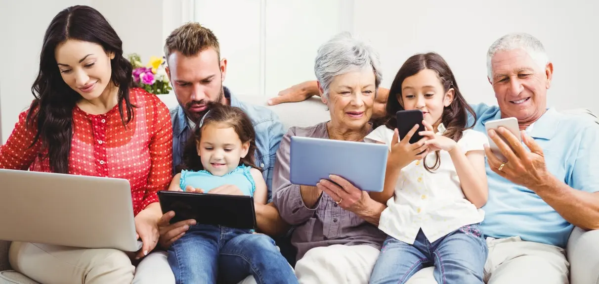 Eine Mehr-Generationen-Familie sitzt gemeinsam auf der Couch vor verschiedenen diditalen Endgeräten