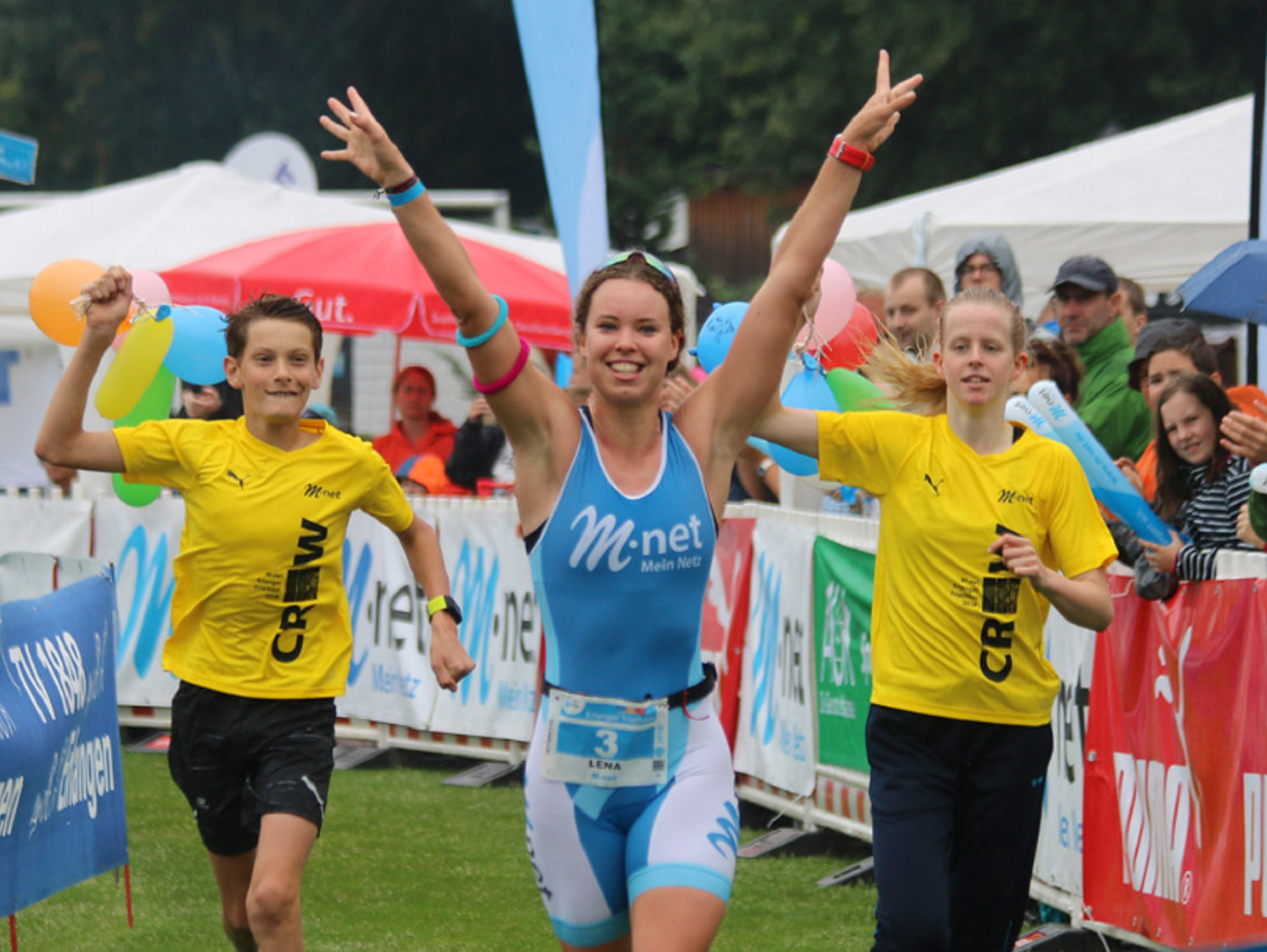 Drei Menschen laufen beim Erlanger Triathlon durch den Zielbogen.