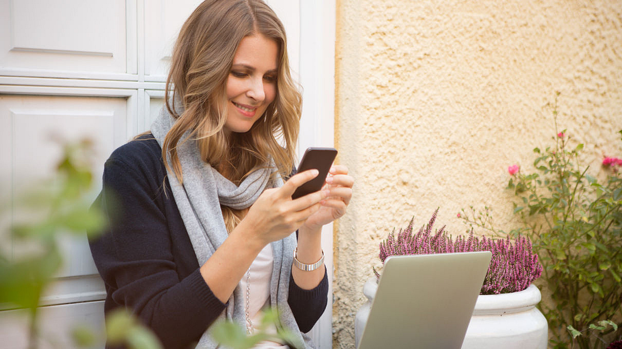 Frau mit einem Mobiltelefon vor einem Laptop