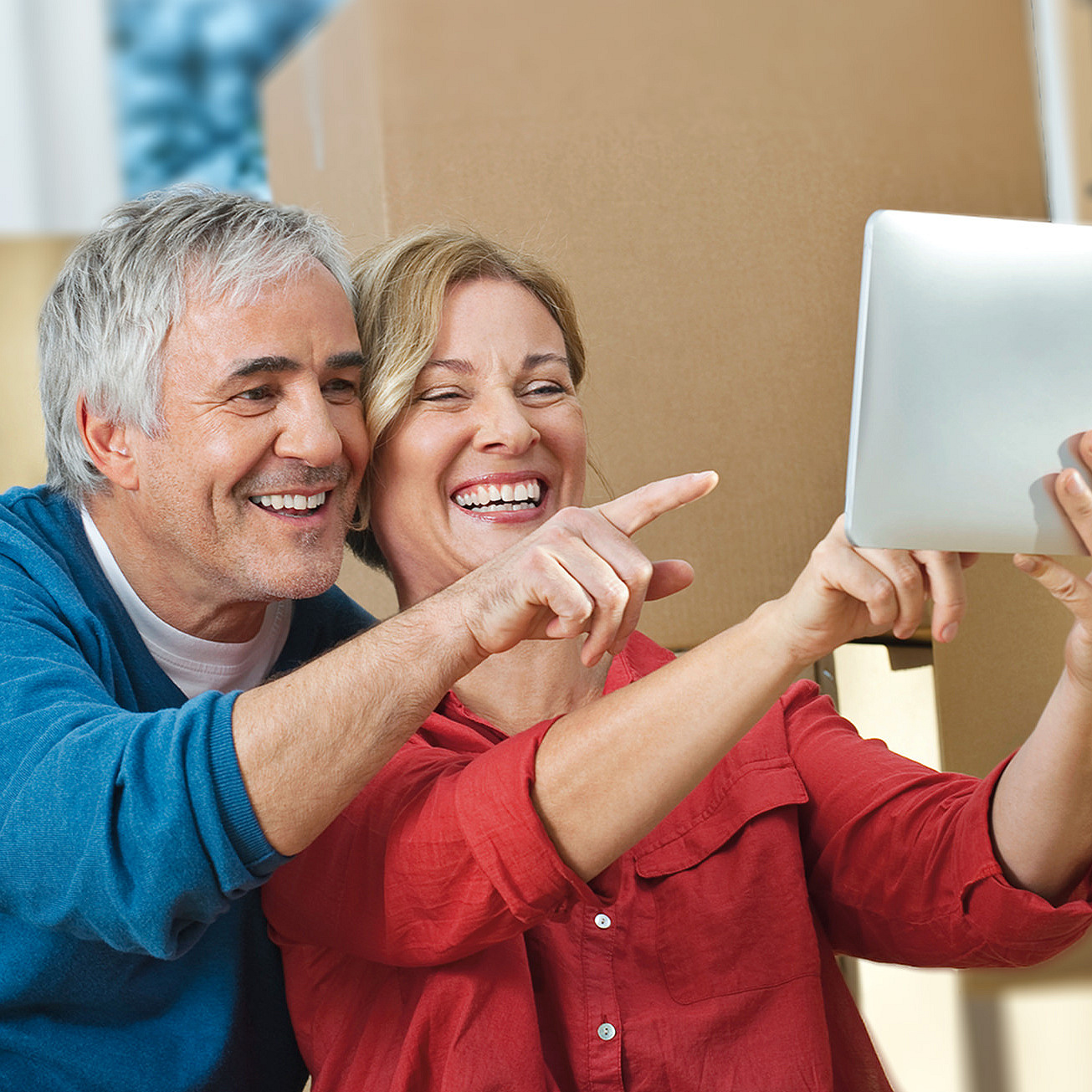 Paar sitzt mit iPad vor Umzugskartons offenbar während eines Umzugs