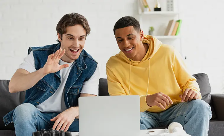 Zwei Männer auf einem Sofa vor einem Laptop scheinbar bei einem Videocall