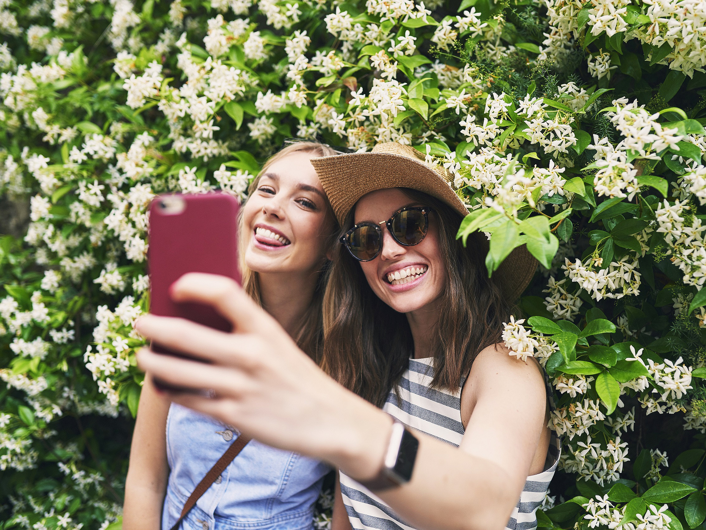 Zwei Frauen stehen vor einer blühenden Hecke und machen ein Bild von sich.