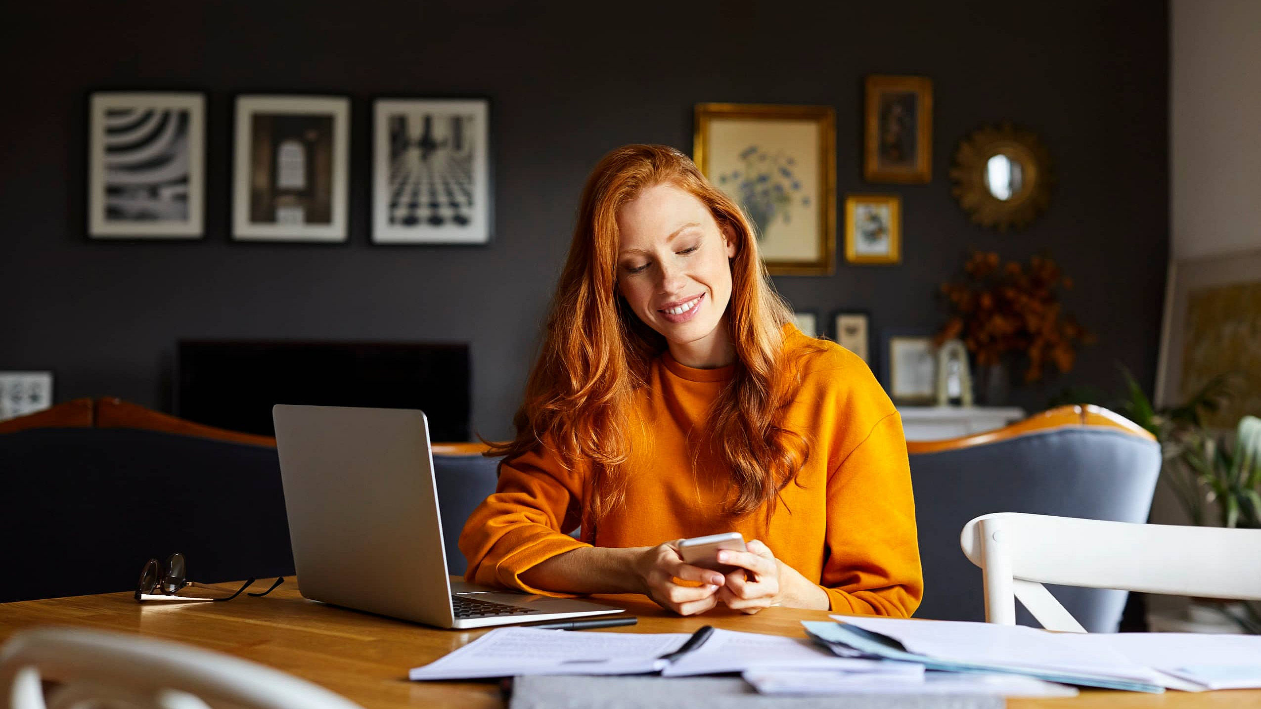 Frau sitzt am Schreibtisch mit Laptop und Mobiltelefon