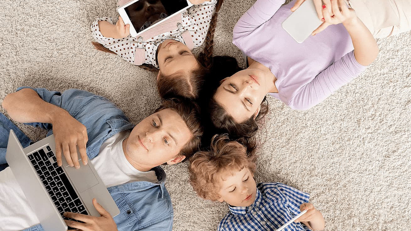 Vier Familienmitglieder auf dem Boden liegend, alle haben ein mobiles Endgerät in der Hand