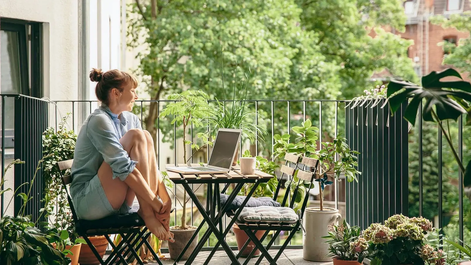 Frau auf dem Balkon vor einem Laptop um sie herum viel grüne Natur