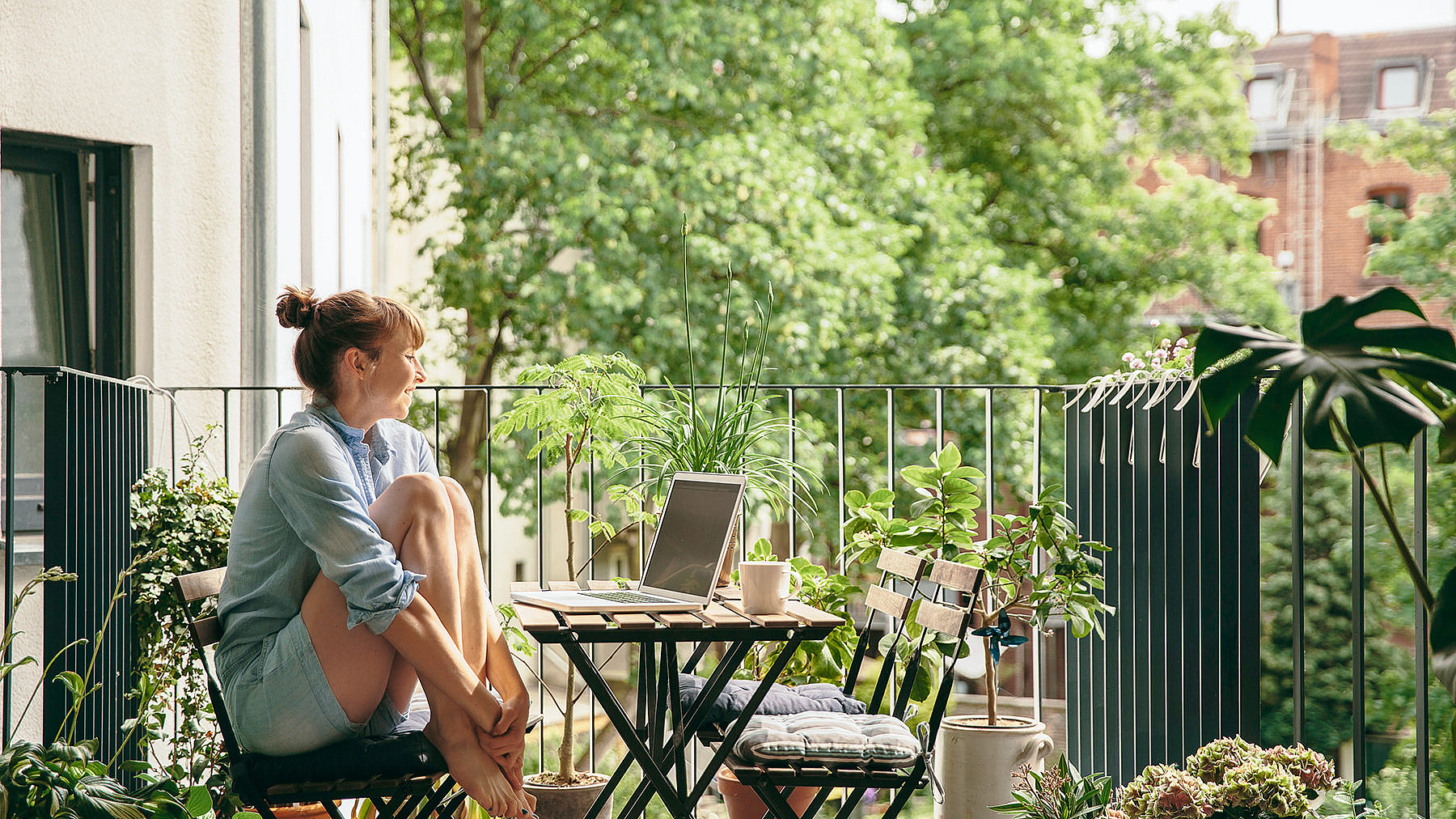 Frau sitzt auf dem Balkon vor einem Laptop um sie herum ist viel Natur