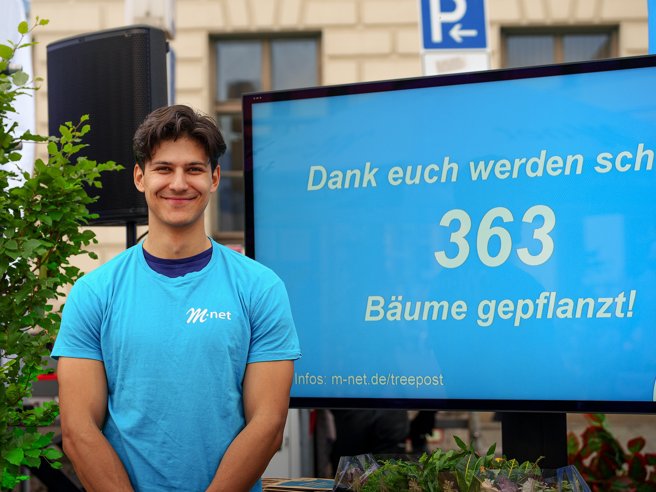 Mitarbeiter vor einem Infoscreen, auf dem die Anzahl der gepflanzten Bäume zu lesen ist