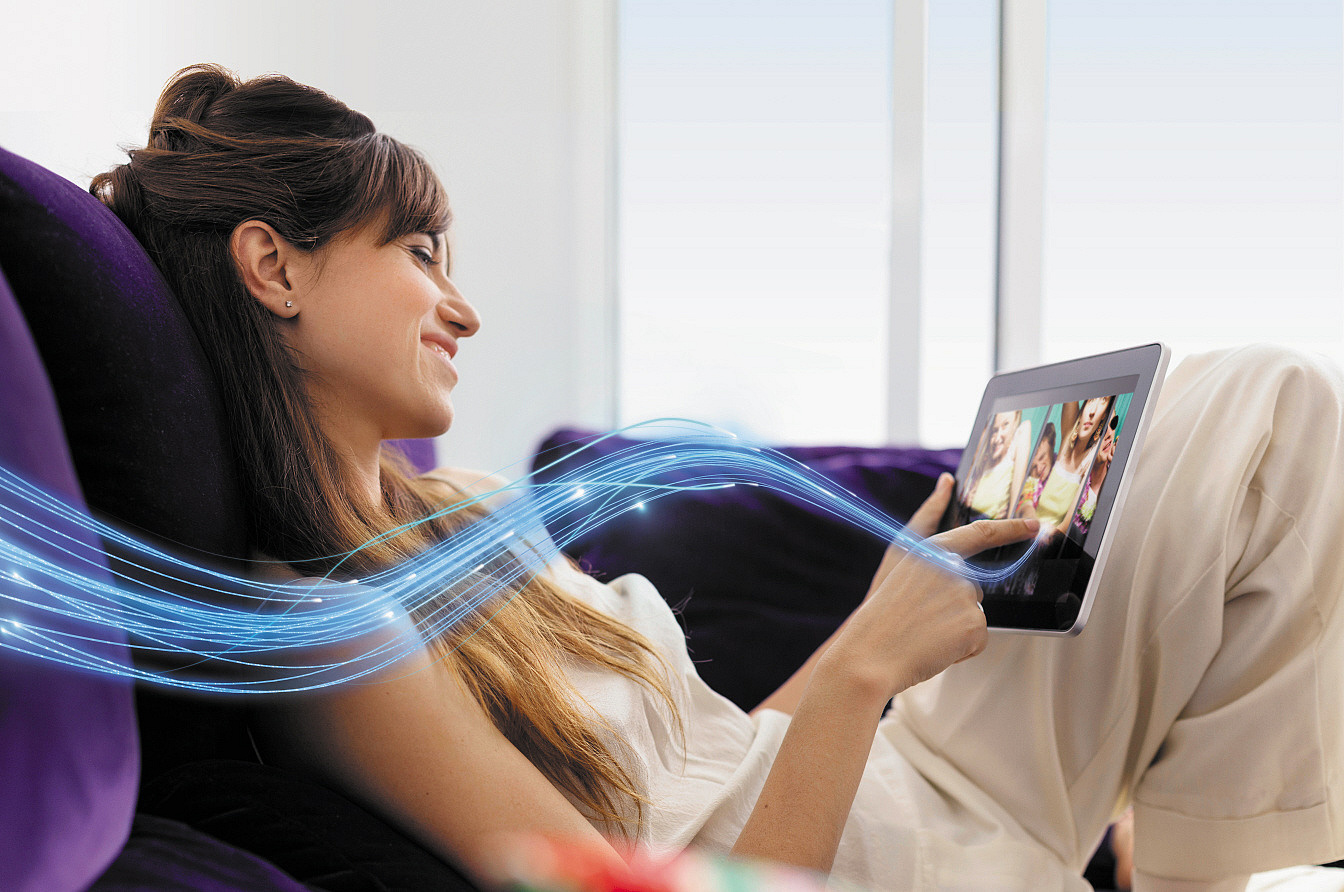 Frau liegt auf dem Sofa mit einem Table, ein Glasfaser Stream symbolisiert FTTH