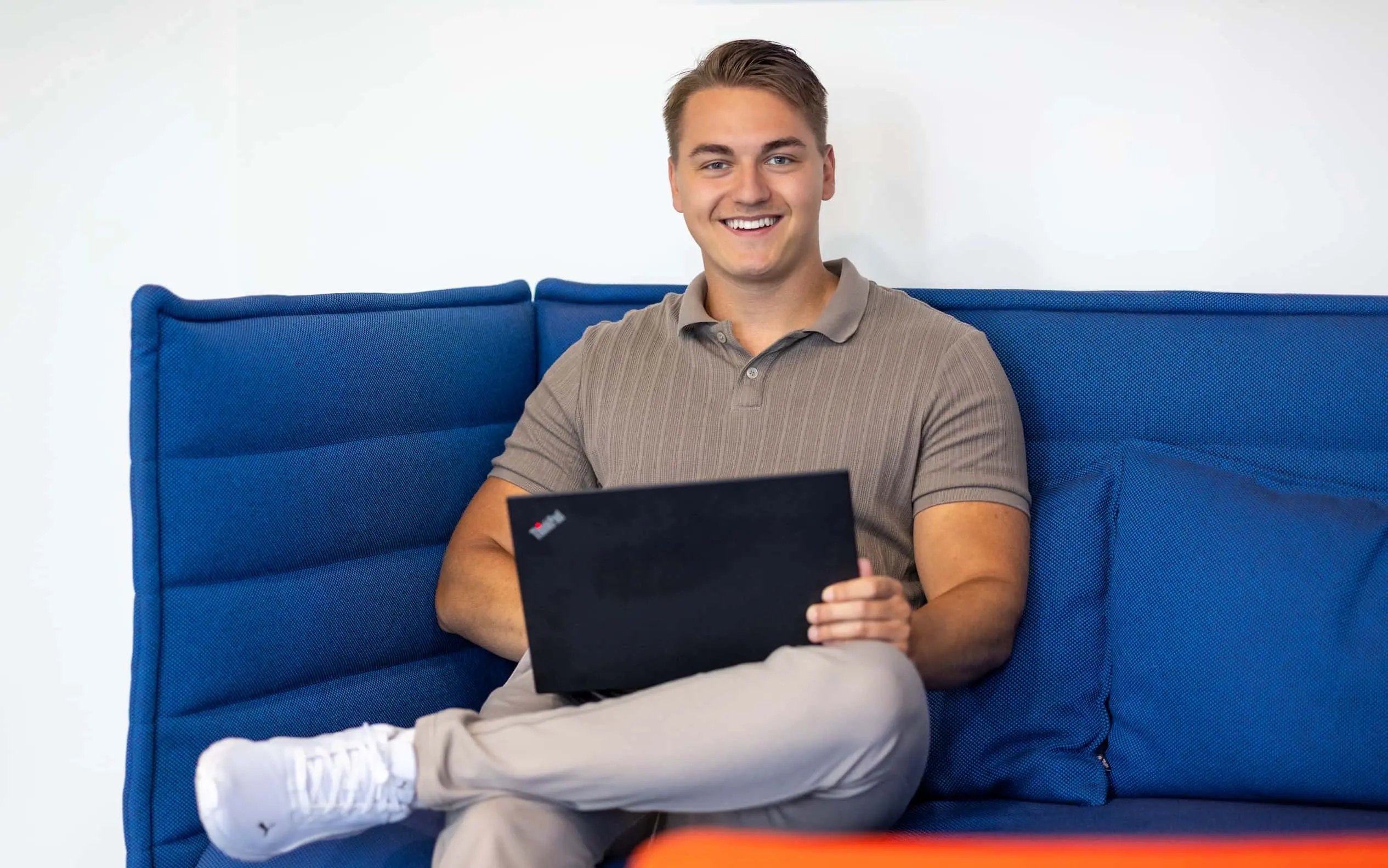 Ein Werkstudent sitzt im M-net Büro auf dem Sofa, auf dem Schoß sein Laptop
