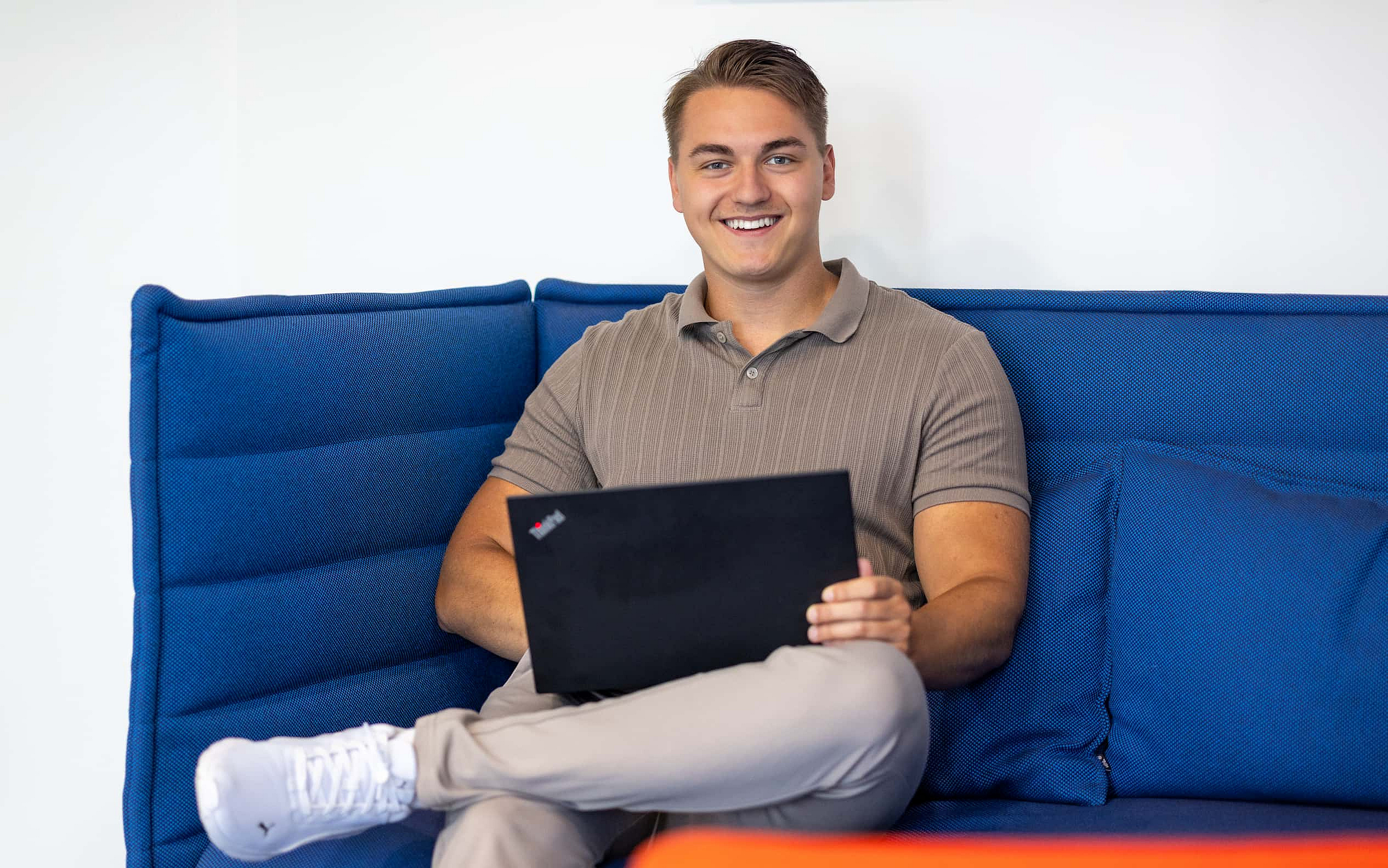 Ein Werkstudent sitzt im M-net Büro auf dem Sofa, auf dem Schoß sein Laptop