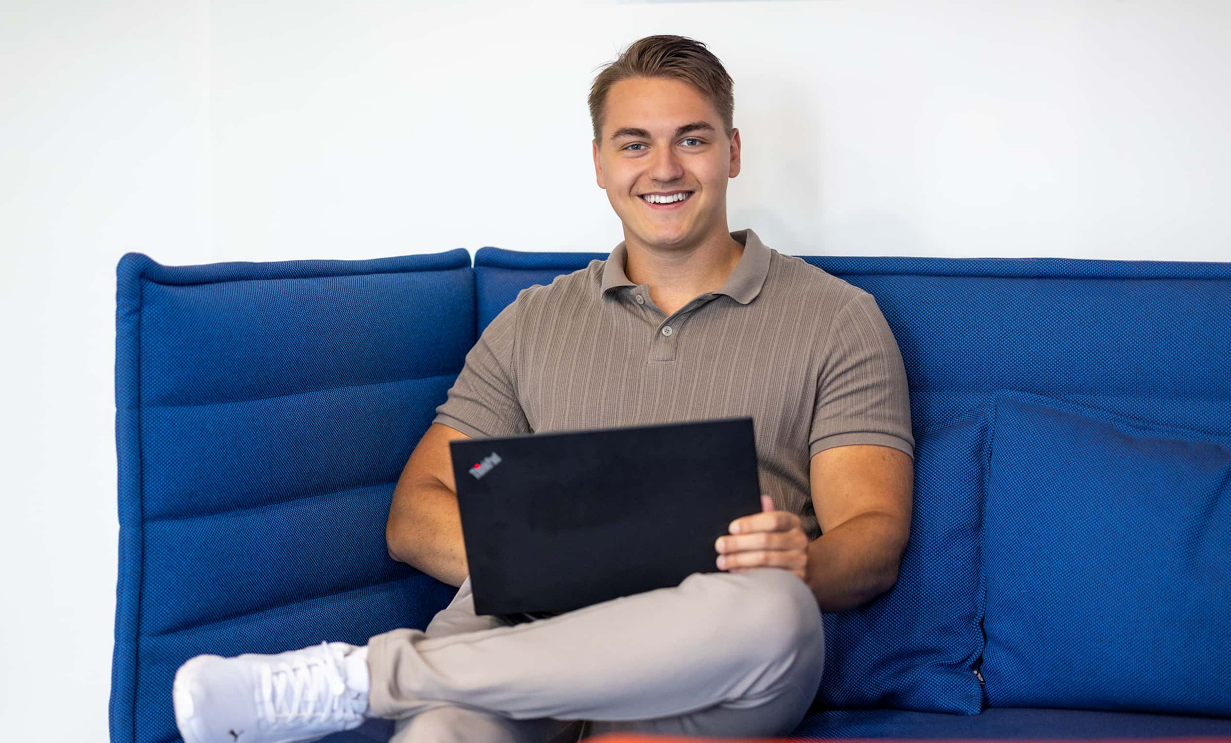 Ein junger M-net-Mitarbeiter sitzt auf der Couch mit dem Laptop auf dem Schoß