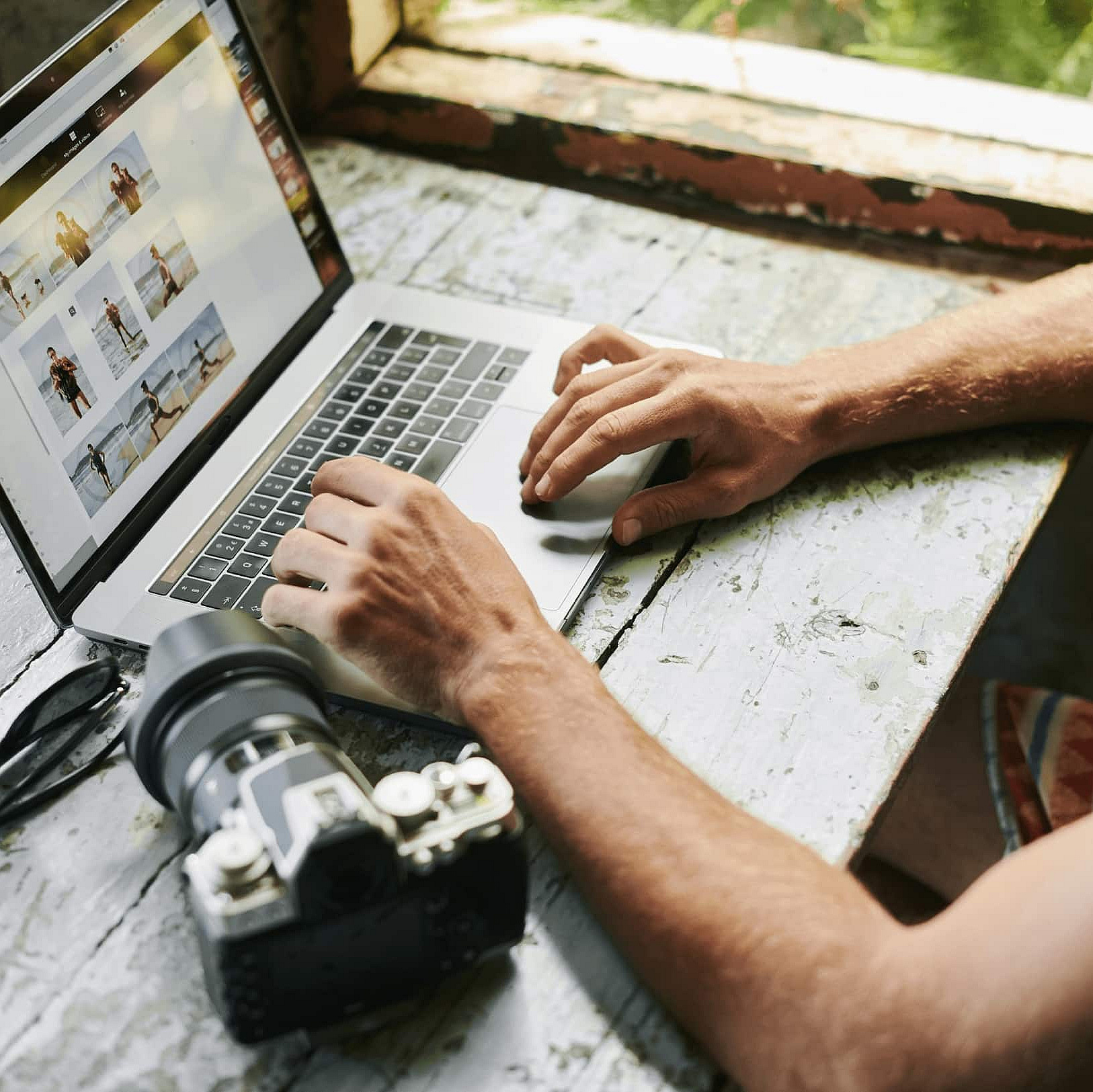 Laptop und Kamera auf einem Tisch, jemand sitzt davor, es sind nur die Hände auf der Tastatur zu sehen