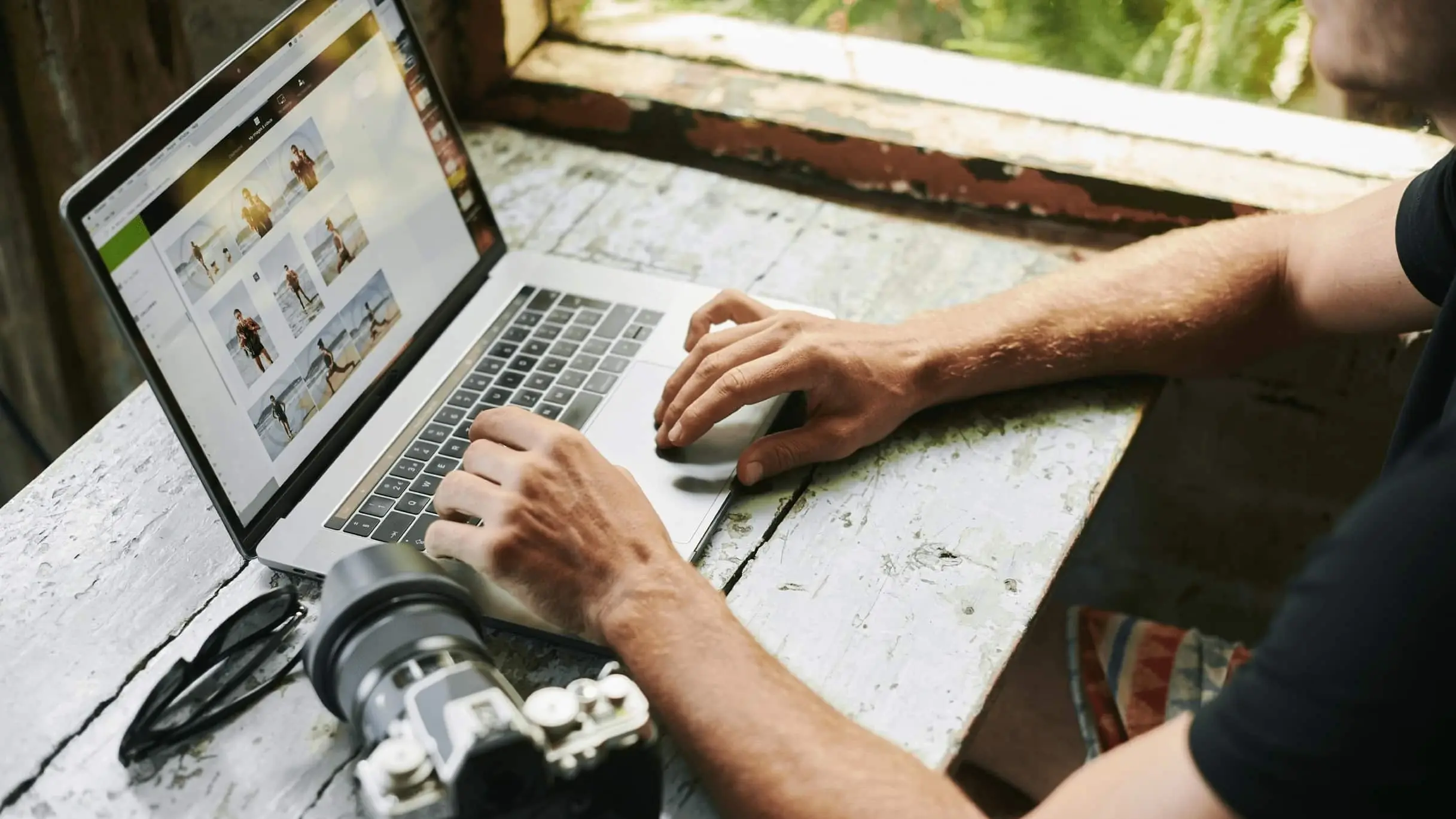 Großaufnahme auf einen Schreibtisch mit einer professionellen Kamera, von der Bilder auf einen Laptop übertragen werden