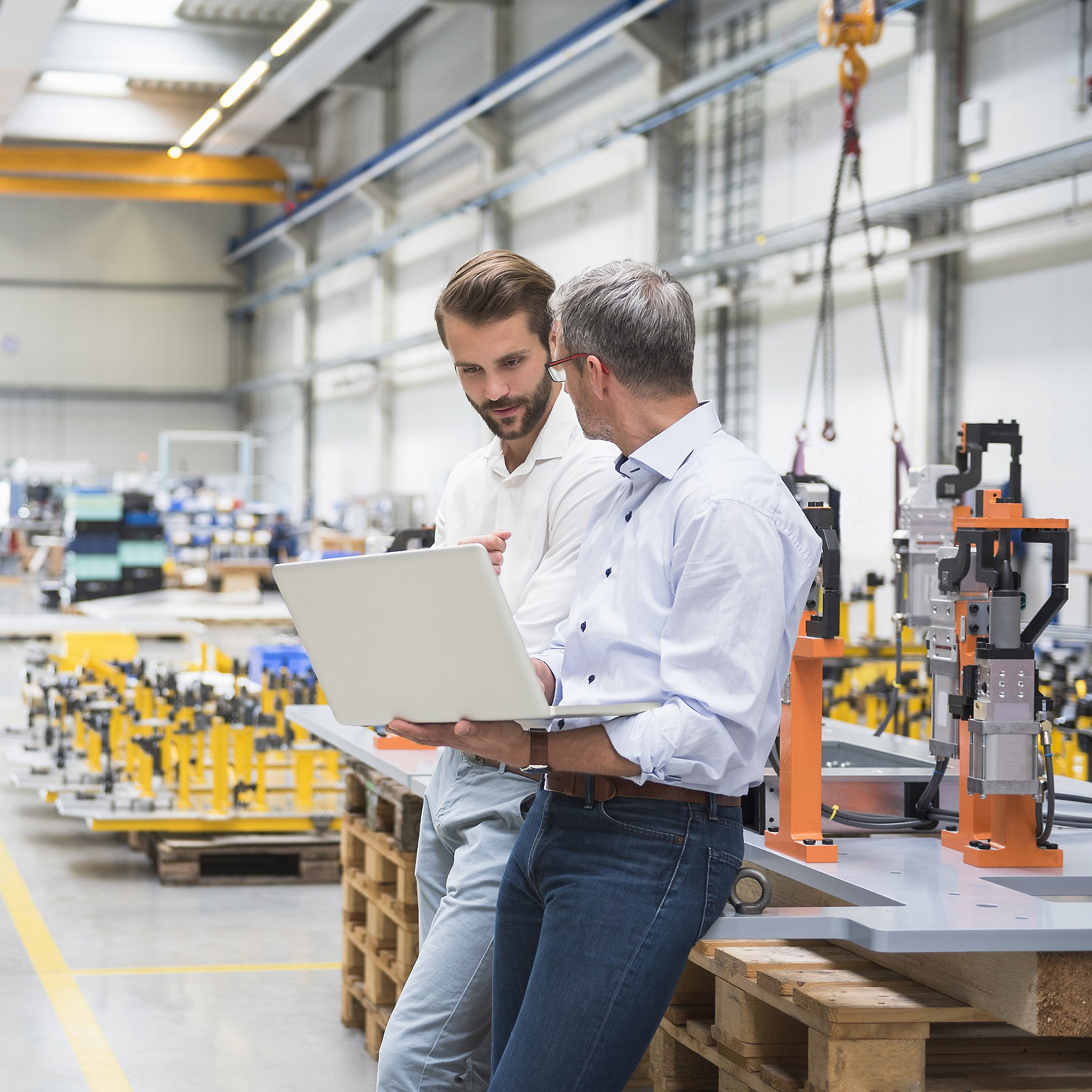 Zwei Mitarbeiter in einer Produktionshalle besprechen sich vor einem Laptop