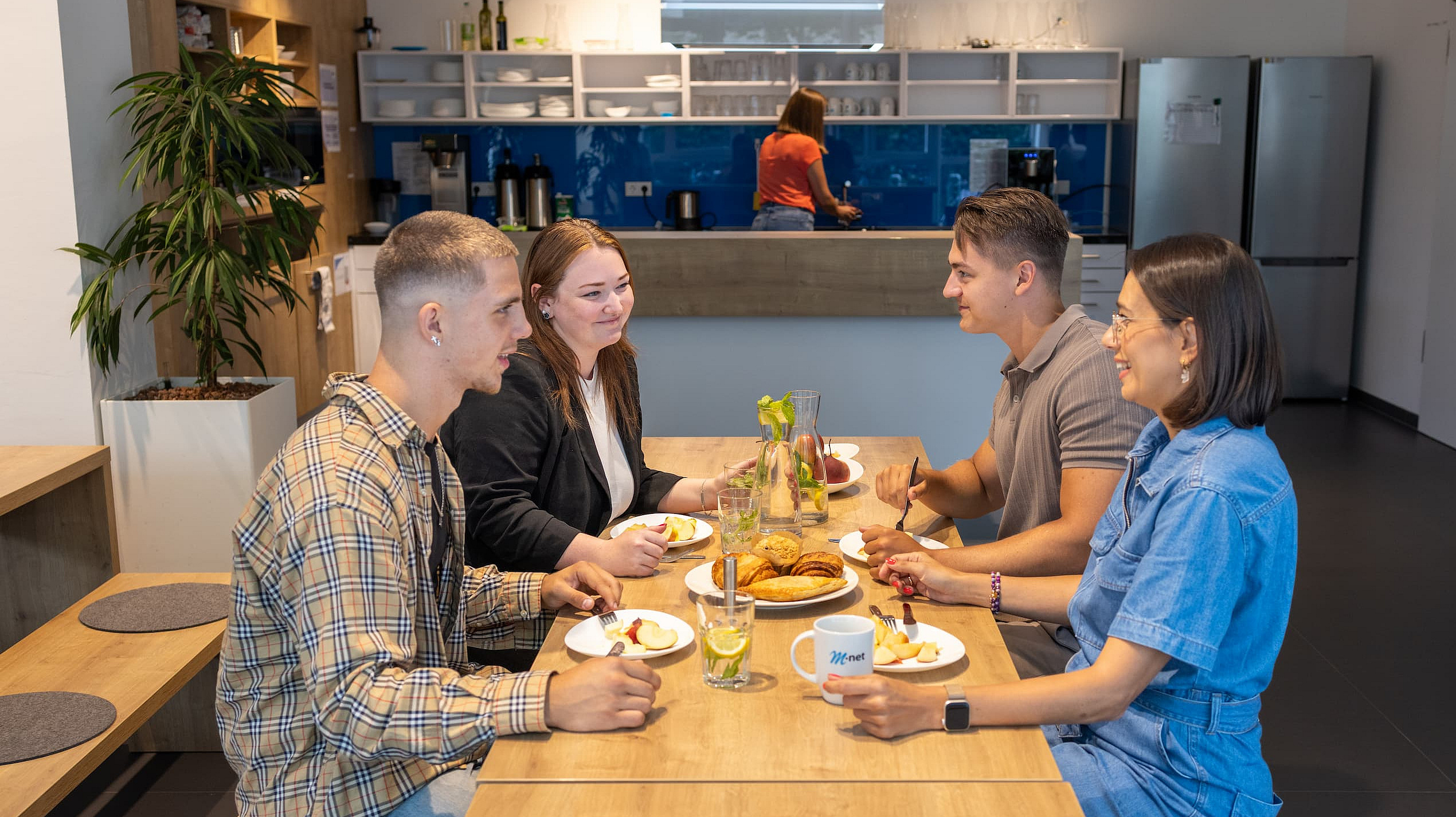 Zwei Kollegen und zwei Kolleginnen von M-net sitzen in der Mitarbeiterküche beim gemeinsamen Frühstück