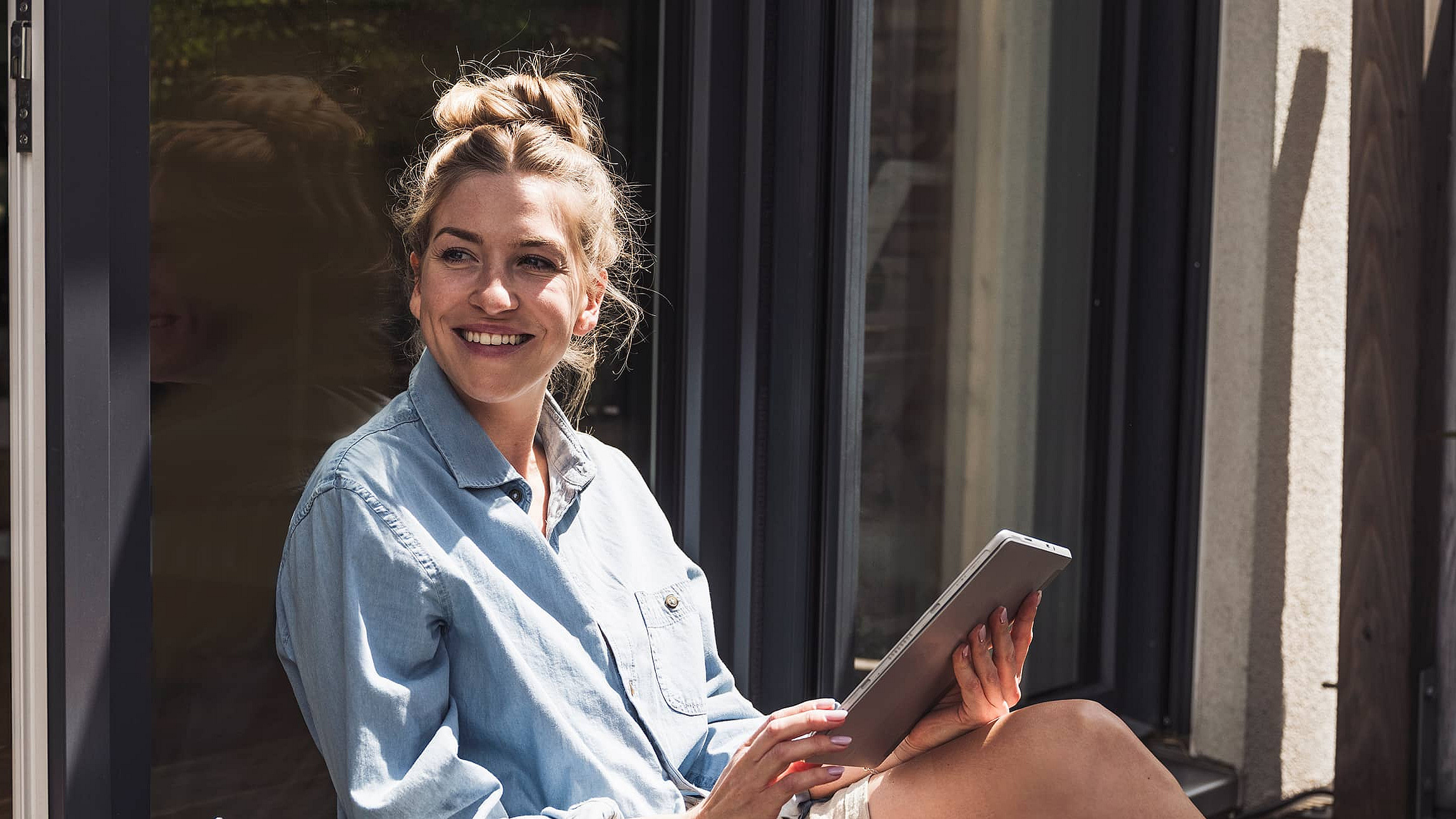 Eine Frau sitzt drau&szlig;en in der Sonne, ein Tablet in der Hand