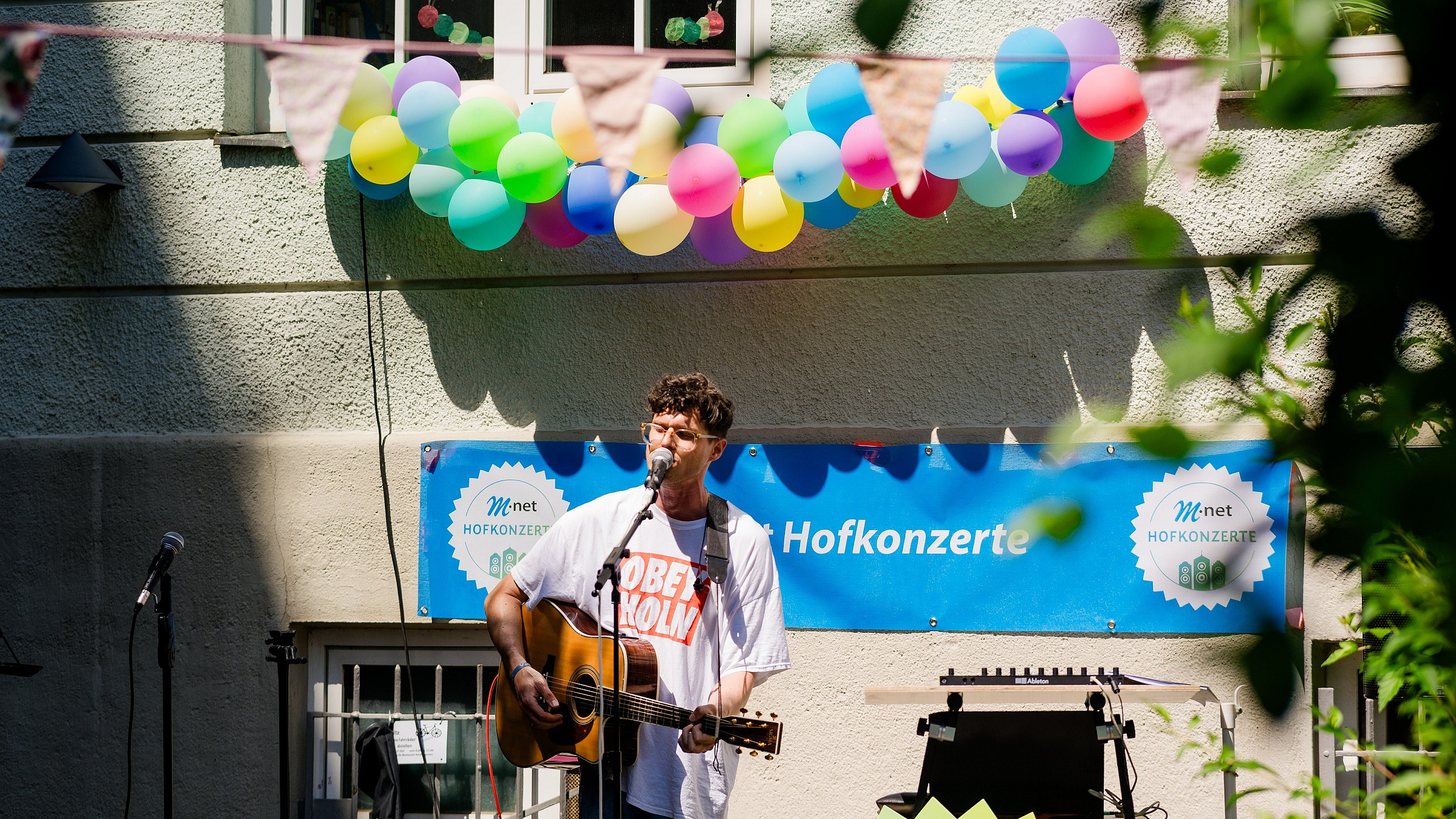 Sänger mit Gitarre vor einem M-net Plakat bei einem Hofkonzert
