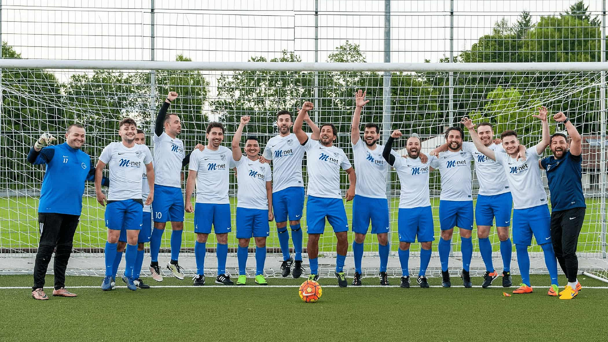 Eine Fußballmannschaft steht in einer Reihe auf dem grünen Spielfeld vor dem Tor. Vor Ihnen liegt ein bunter Fußball.