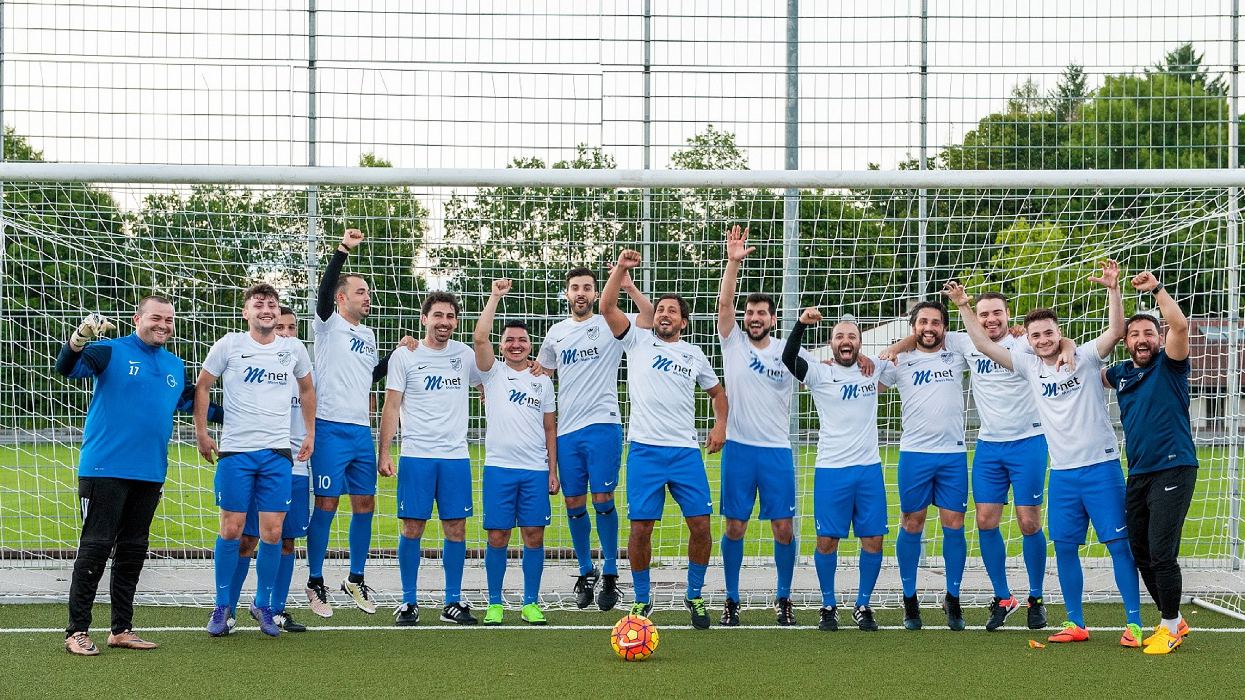 Fußballmannschaft in M-net Trikots stehen vor einem Tor