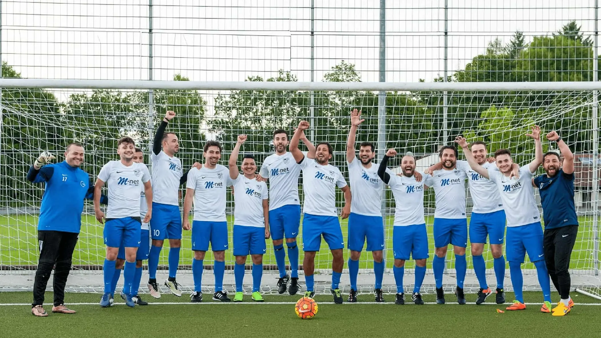 Fußballmannschaft in M-net Trikots stehen vor einem Tor