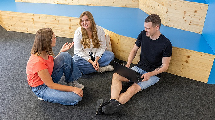 Drei Kollegen von M-net sitzen zusammen auf dem Boden und besprechen sich