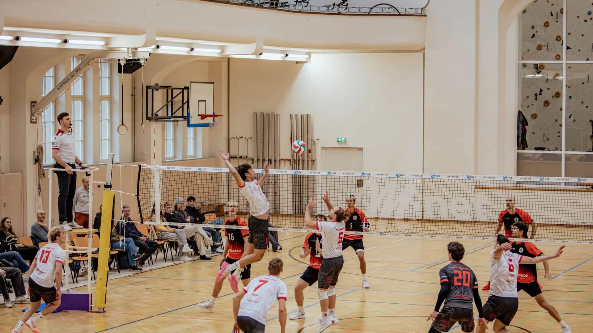 Zwei Mannschaften spielen in einer Turnhalle Volleyball