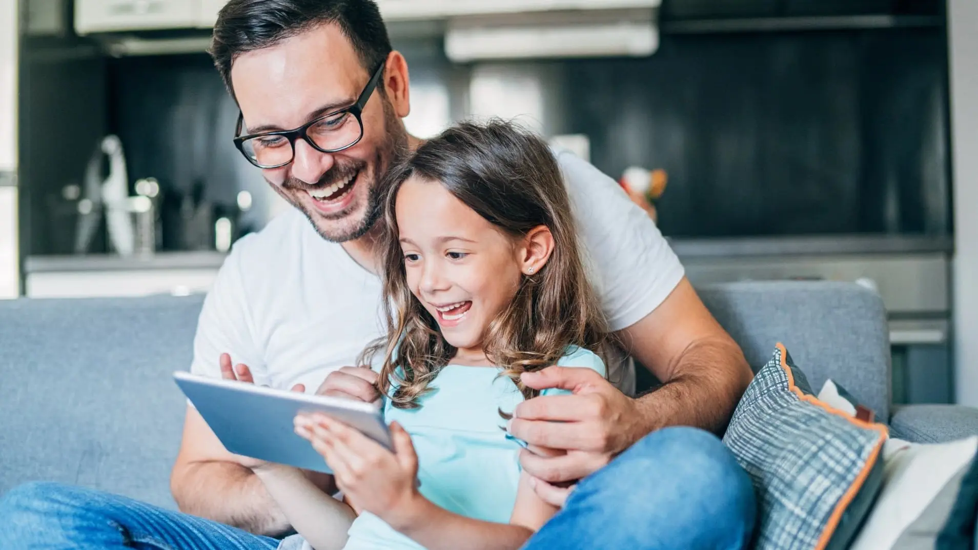 Ein Vater und seine kleine Tochter sitzen gemeinsam vor einem iPad